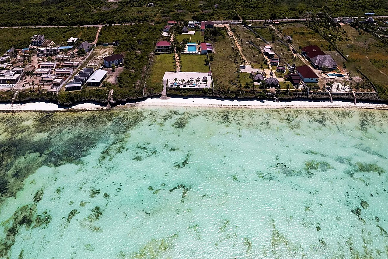 Overhead view straight down onto the empty white sand and shallow water of the Jambiani flats at low tide.