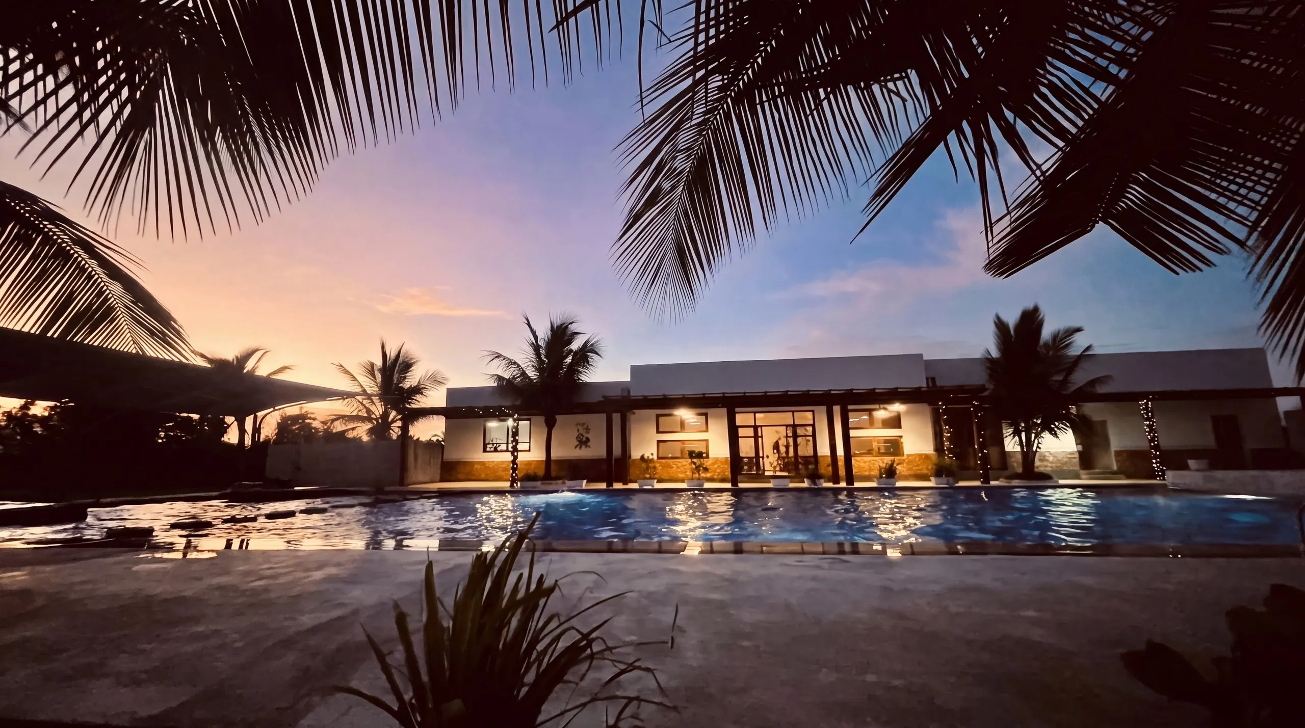 The pool bar and terrace lit at dusk, reflected in the pool, Raffia Boutique Hotel