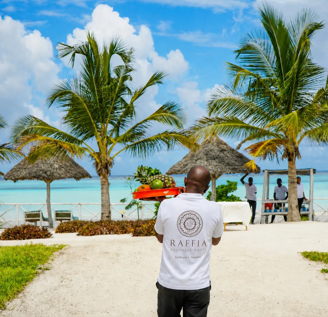 A member of the Raffia team carrying fresh fruit down to the beach, with the lagoon beyond